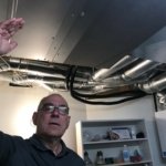 Michael Overend stands under the manifold where the heat pump refrigerant comes in and warm air is sent to several rooms through ductwork.